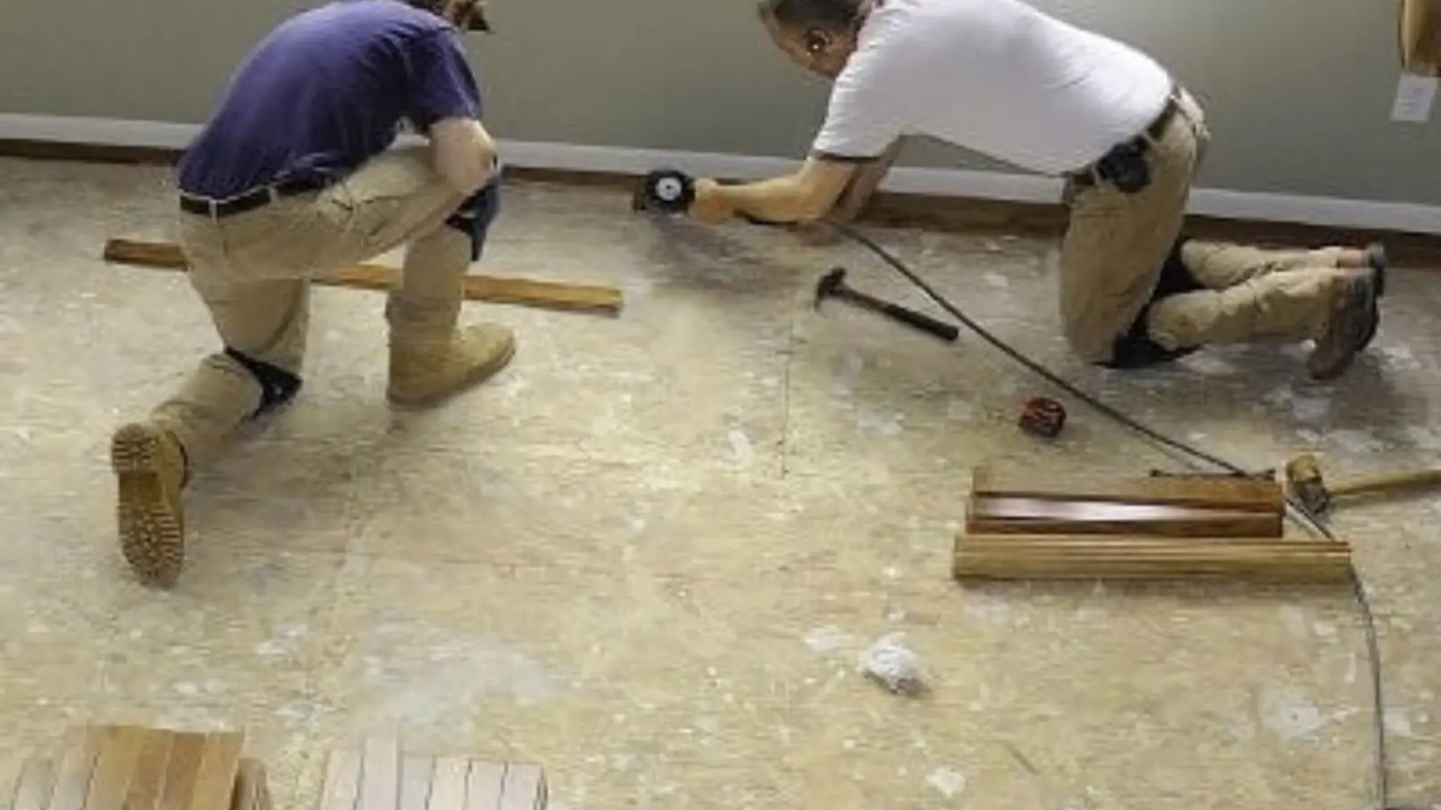 Two workers kneeling on a floor installing new flooring during a water damage repair